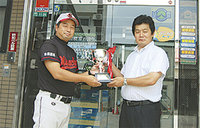 久野社長（右）から星野さんへ優勝カップ等が贈られた（同社前にて）