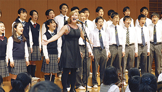 桐蔭学園の演奏を指揮するケリーさん（右写真）と、生徒らと合唱するアンダーソンさん
