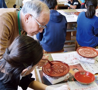 漆を塗る斉藤さんと児童