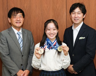 メダルを２つ持つ石黒さん（中央）と溝上理事長（右）、岡田校長（左）