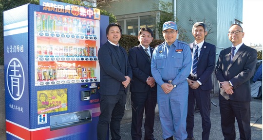 取材に応じた花岡さん（中央）と（株）八洋の担当者ら。左はオリジナルラッピングの自動販売機