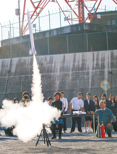 空へと昇るロケットを見守る植松さんと生徒たち