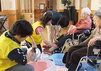 岩手県大槌町で高齢者の足浴を手伝う明学大生