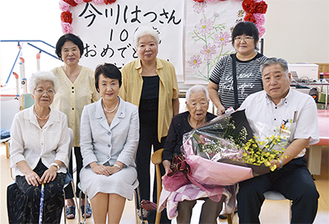 花束を手にする今川はつさんと家族。前列右は津田区長、前列左から２人目が林市長。