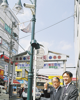 設置したカメラのもとに立つ加藤理事長（左）と中田支店長
