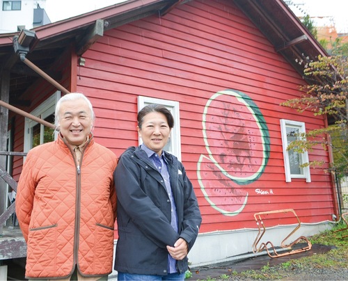 土志田さん（左）と参加アーティストの一人、橋村至星さん。橋村さんが赤い家に描いた作品『ボーダーラインを歪めるために』の前で