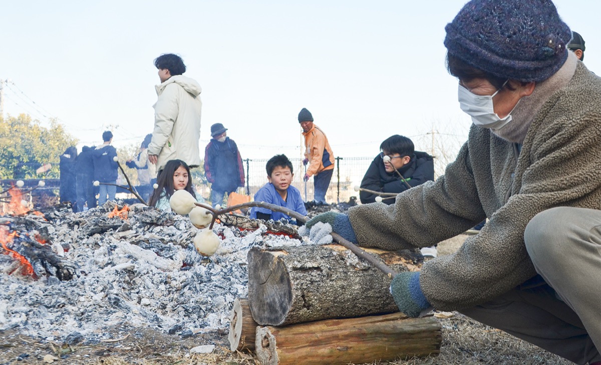 丸太を支えにして、握りこぶし大のだんごを焼く女性