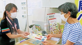 笑顔でセットを手渡す局員（８月31日、神奈川菊名郵便局）