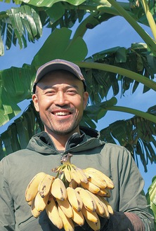 露地栽培に成功したバナナを手に笑顔を見せる古川原さん