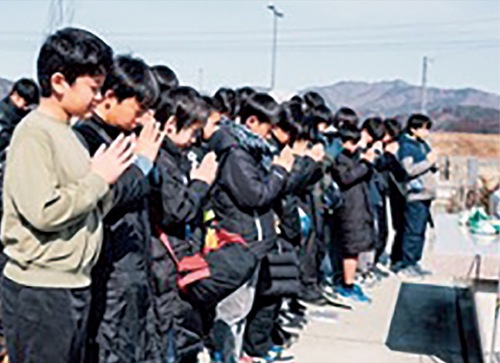 震災遺構の大川小学校で手を合わせる選手たち＝提供写真