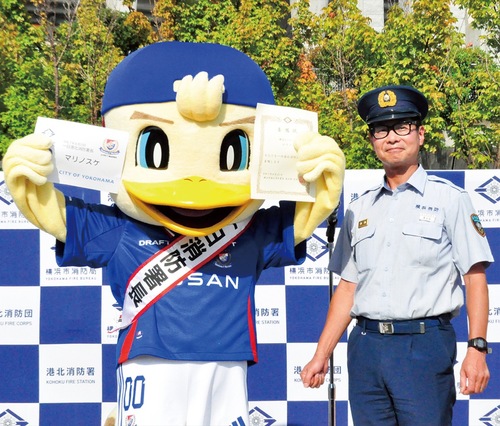 長谷部署長（右）から手渡された委嘱状と名刺を掲げるマリノスケ