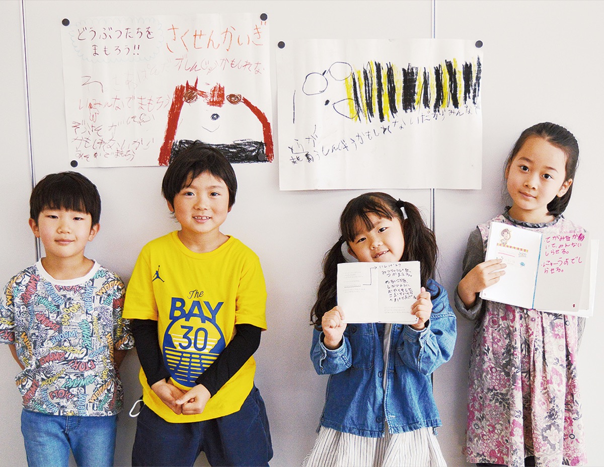 手作りのポスターやノートを見せる４人