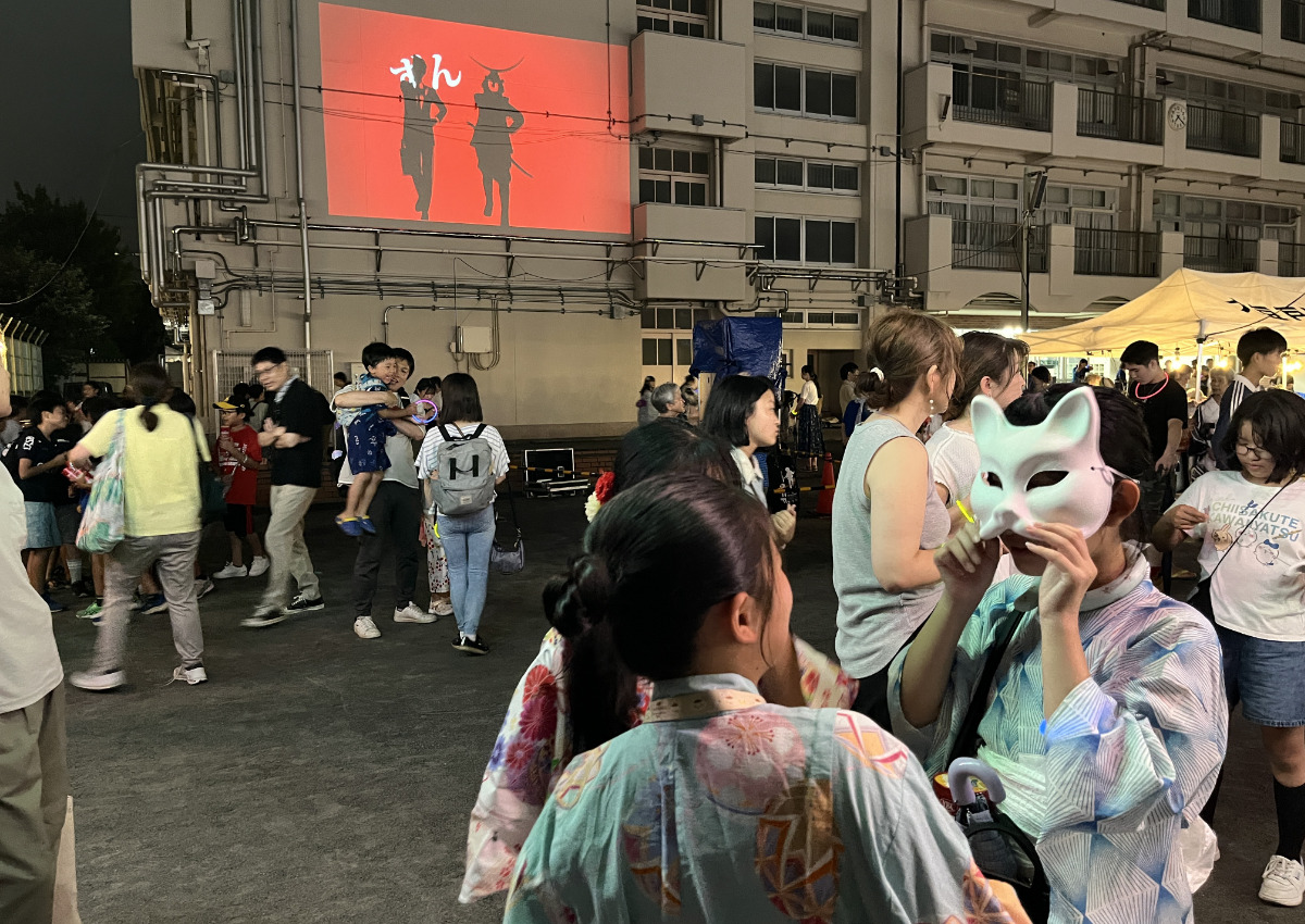 踊りの楽曲に合わせた映像と、お面をかぶりはしゃぐ来場者ら