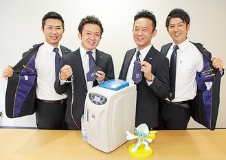 五輪エンブレムが光る、ＡＯＫＩのスーツ。ドクターズ・マンの営業マンが着用している。写真手前は、同社が日本国内で開発した新商品の水素吸引機（Ｈ２ＪＩ１）