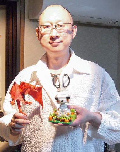 レゴブロックで作ったハサミ立てと折り紙で作った龍の「ワイバーン」を持つ山倉さん