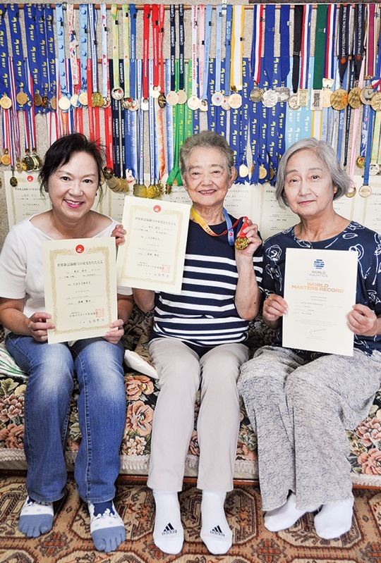 部屋には数多くのメダルが並ぶ。米沢さん（中央）を支えている佐伯さん（右）と和美さん