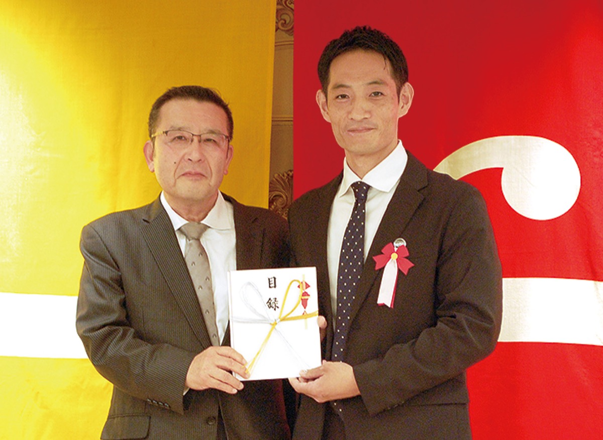 西村実行委員長（左）から目録を受け取る現顧問の飯塚貴行さん