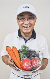 収穫した野菜を手に笑顔の二谷さん