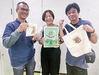 記念誌を持つ名和さんを中心にエコバッグを持つでっかいそらの石井聡さん（左）と望月孝敏さん
