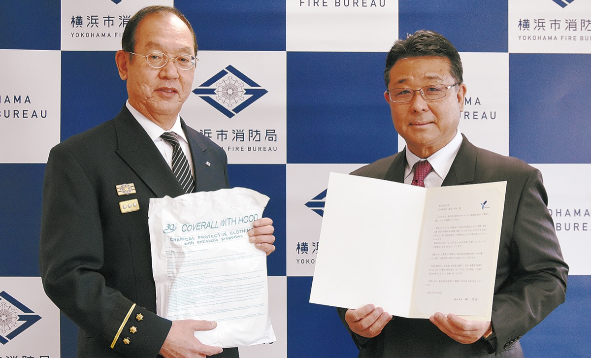 防護服を手に持つ松原局長(左)と飯島社長