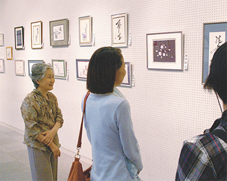 展示作品を説明する山崎さん（左）