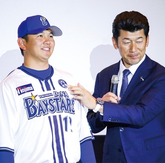 三浦監督（右）から投手キャプテンのマークを託される山崎選手