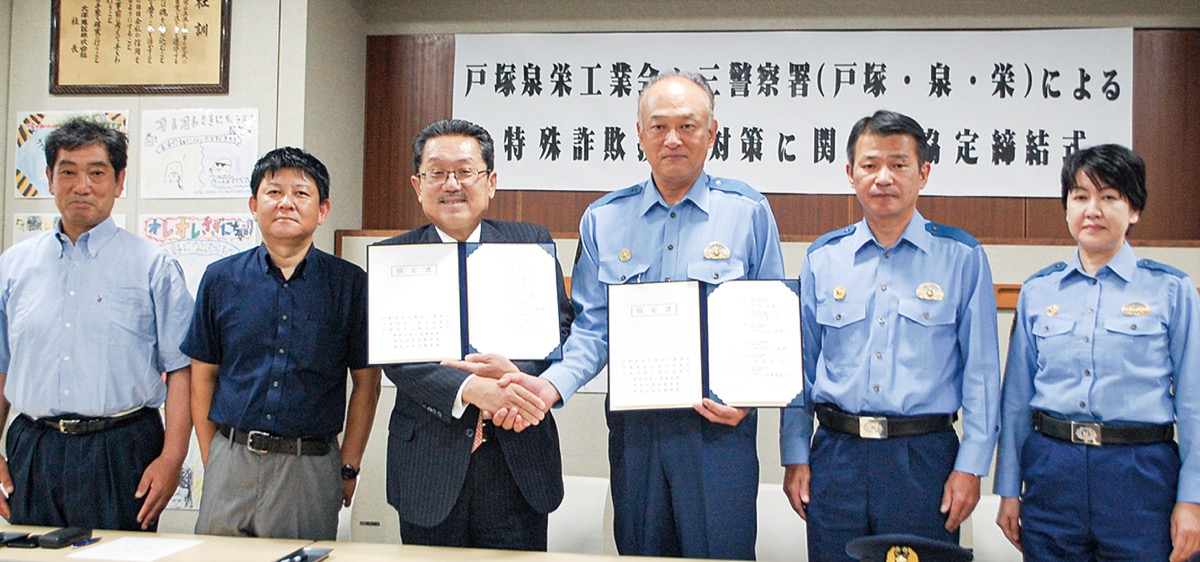 協定書を持ち握手を交わす黒田会長（左）と戸塚署の村上滋敏署長