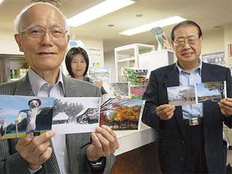 絵はがきを手にする田島連絡会会長（左）と清水さん（右）、売店スタッフ