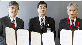 協定書を掲げる葛西区長（中央）、吉村（左）・鎌田（右）支店長