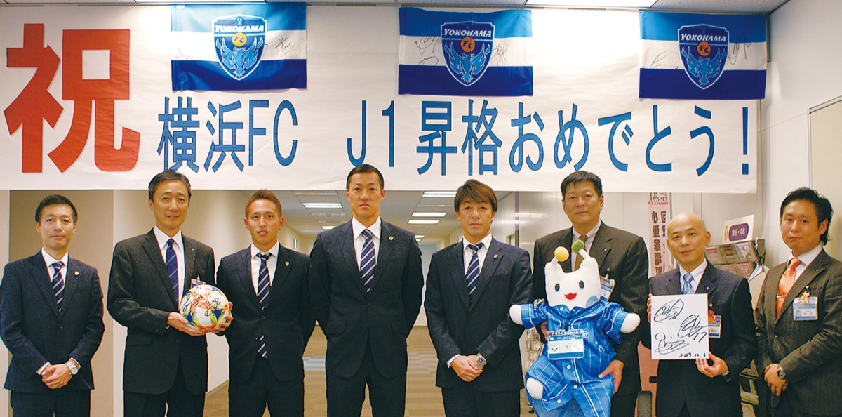 祝賀の横断幕の前に立つ(左から)上尾社長、吉泉区長、武田選手、南選手、下平監督と区役所職員