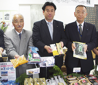 自慢の商品を手にする和田・共栄会理事長（左）、須田・女川町長（中央）、長田・建築安全協会理事長