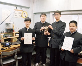 校内の無線室で賞状や盾を持つ４人