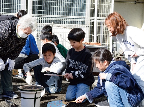 七輪を見つめてうちわであおぐ児童たち