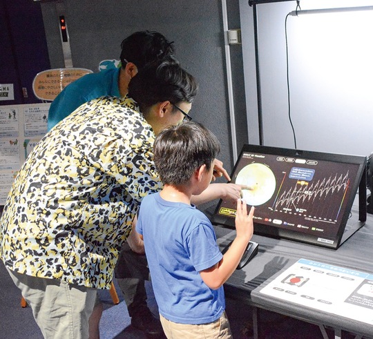 装置に触れて温室効果ガスの濃度を見る親子