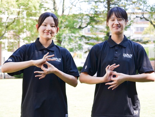 デフリンピックを表す手話ポーズをとる志希さん（左）と志野さん