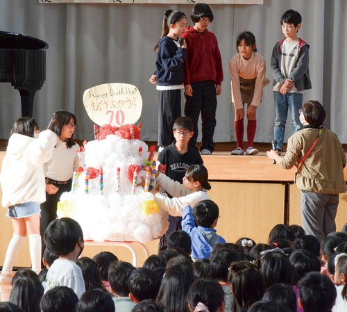 大きなケーキにろうそくを立てる児童たち