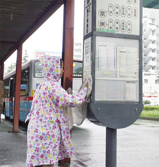 雨の中、バス停を拭き掃除する隊員