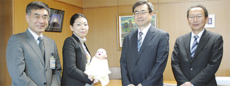 鈴木所長から受け取った人形を抱く担当者（中央左）