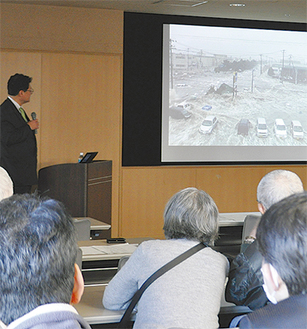 津波の様子を映像で説明する青木さん（左奥）