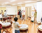 田中さん（右）を囲む形でみんなで太鼓の練習