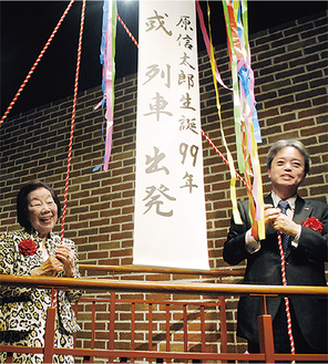 出発を祝いくす玉を割る原美津子館長（左）とJR九州の古宮常務取締役