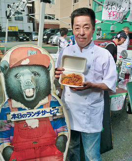 当時の店先にあったクマの看板と一緒に小澤さん
