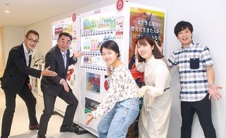 ポスターて掲示した自販機前でルカリス（女性２人）と山本支店長（左から２番目）ら