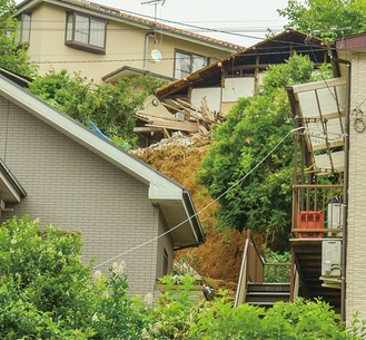 崖崩れが起きた上部の住宅を取り壊し、ブルーシートで覆うなどの対策が検討されている＝5月20日撮影