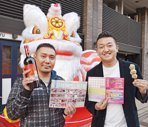 吉田町通りの巨大ランタンの前でスタンプラリー用紙と商品を手にPRする山下理事長（右）と倉本さん