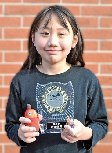 表彰盾とお気に入りのロボットの人形を手にする折田さん