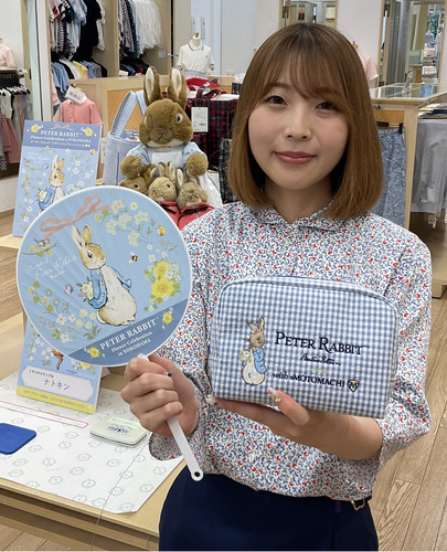 コラボ商品の一つであるポーチとノベルティのうちわを手に、フクゾー洋品店のスタッフ