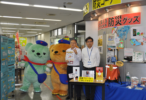 横浜港郵便局２階ロビー内に設置された防災コーナーの前で上遠野局長（左）と市総務局地域防災課長の河合さん