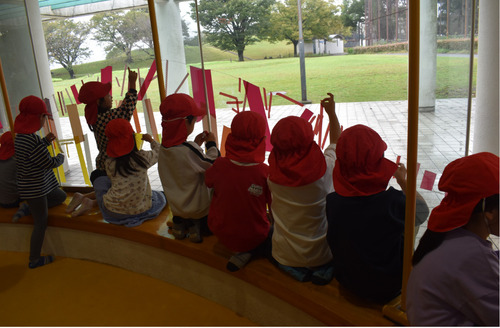 赤、オレンジ、黄のマスキングテープを窓に装飾する園児