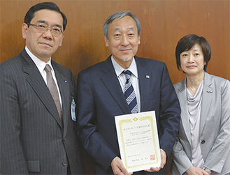 柏崎誠副市長（左）から指定書を受け取った康井総長（中央）と長場直子副院長